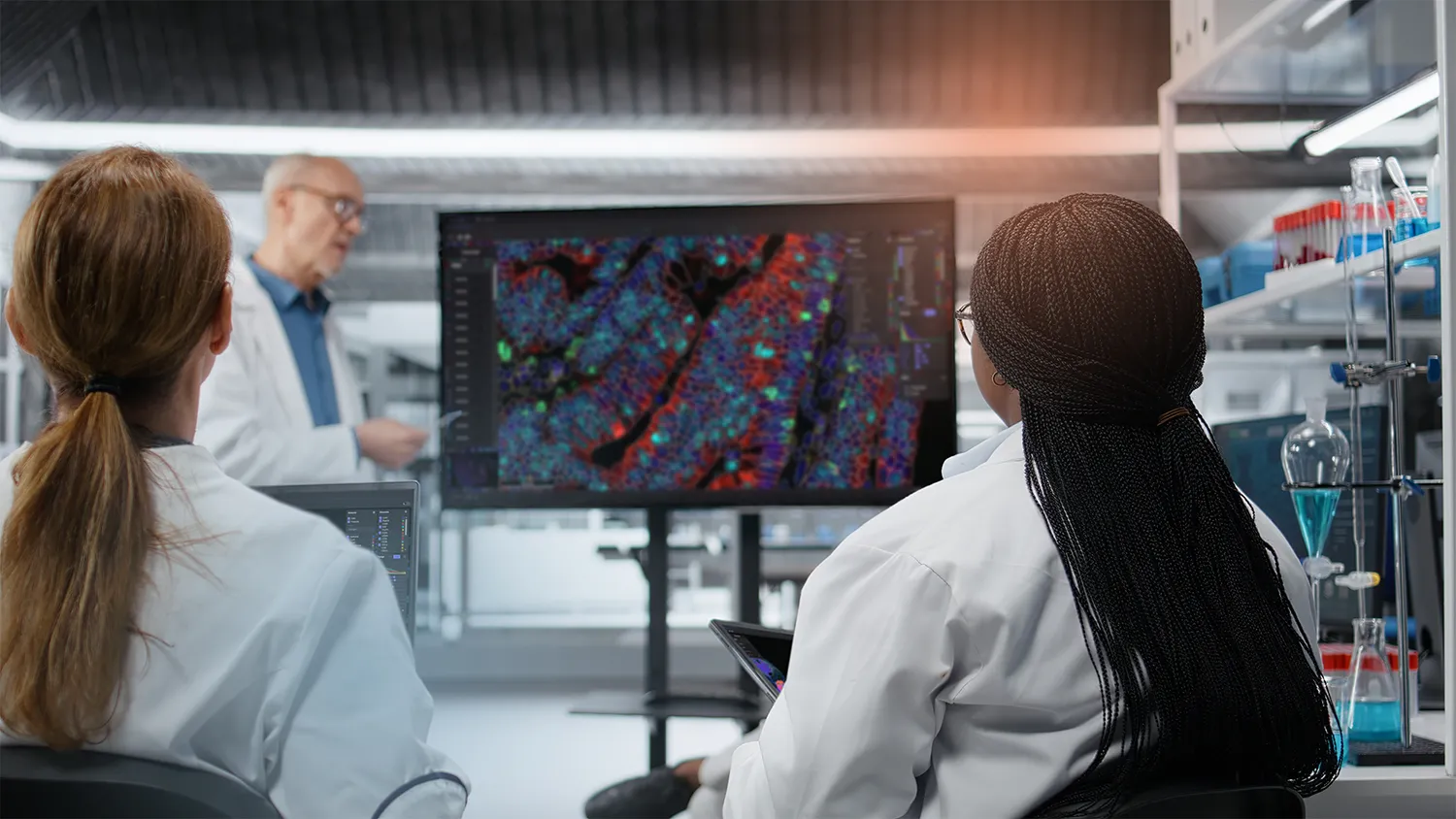 Two scientists discuss a stained tissue image on a large screen in the lab.