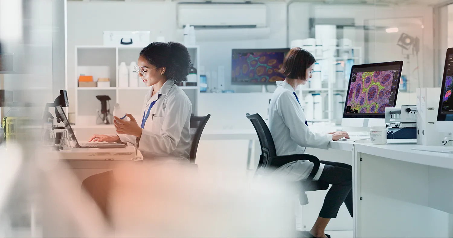 Scientists work at desks with monitors showing tissue images in an open laboratory.