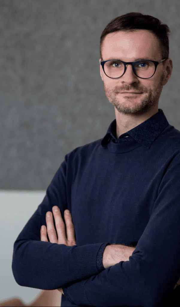 Portrait of Falk Zakrzewski with glasses and a dark shirt, arms crossed.